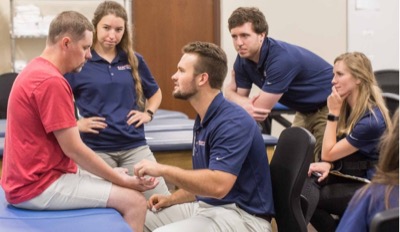 man receives physical therapy while fellow students watch